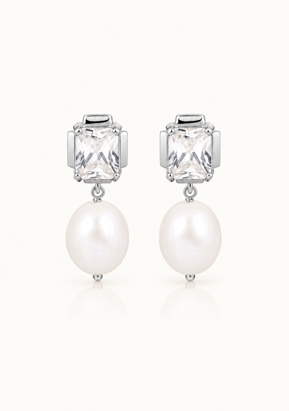 A pair of silver-toned drop earrings featuring a rectangular clear faceted gemstone and a dangling white pearl, shown on a clean off-white background.