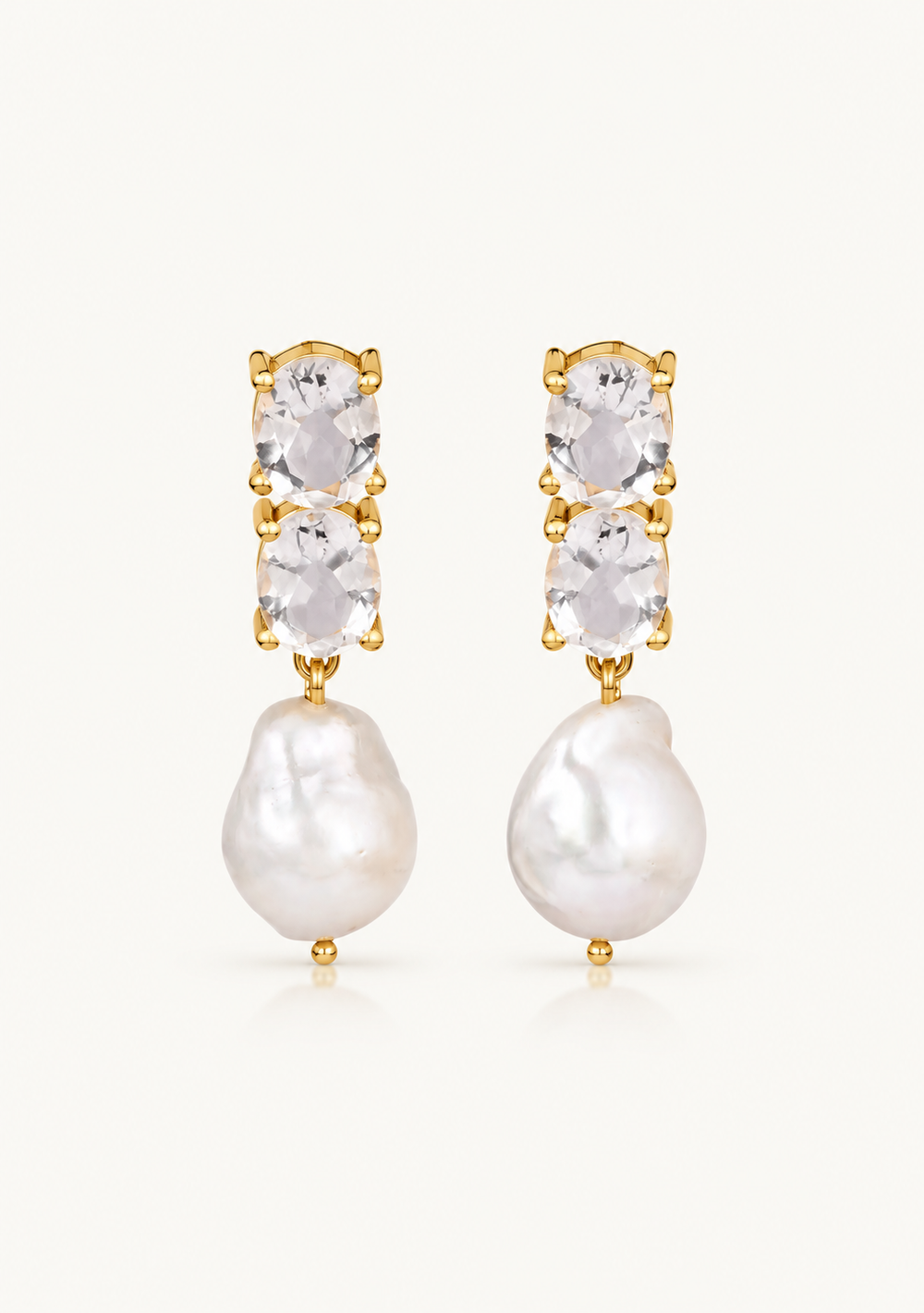 A pair of gold drop earrings featuring three clear oval-cut stones stacked vertically above a large, irregular white baroque pearl, set against a plain off-white background.