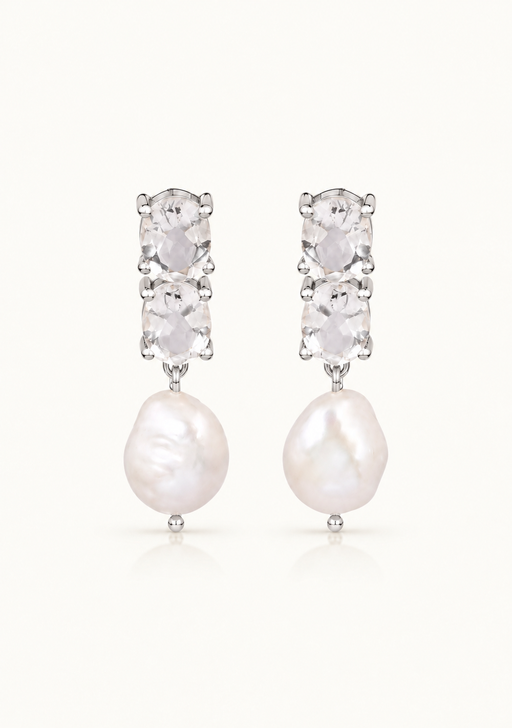 A pair of silver drop earrings featuring three stacked clear oval-cut stones above a large, irregular white baroque pearl, set against a plain white background.