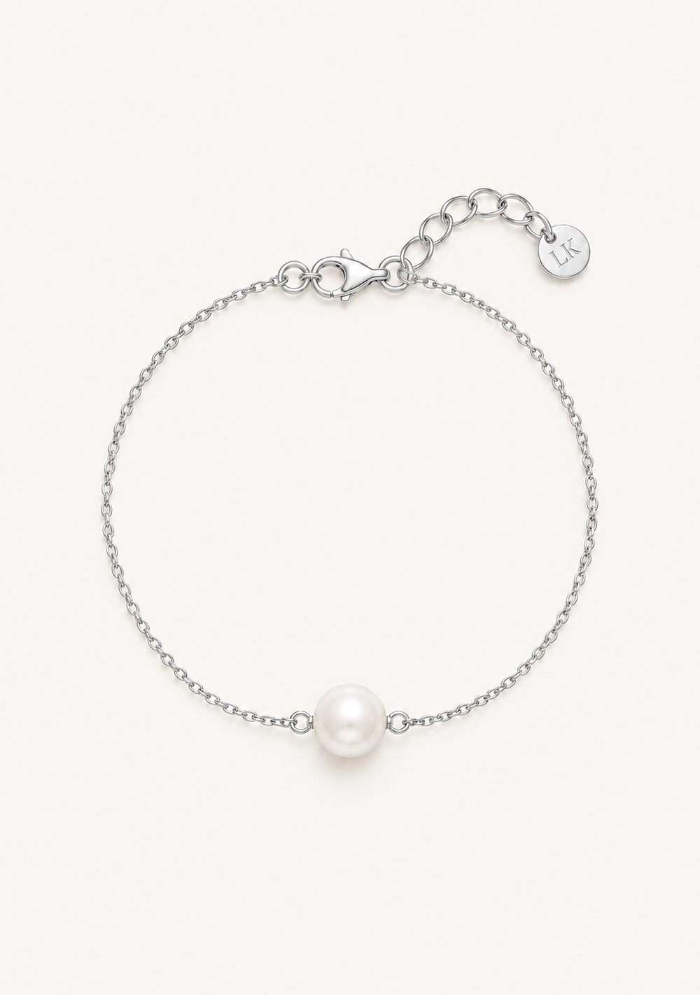A delicate silver chain bracelet featuring a single white pearl bead at the center, with a lobster clasp, extender chain, and a small round engraved charm on a plain white background.