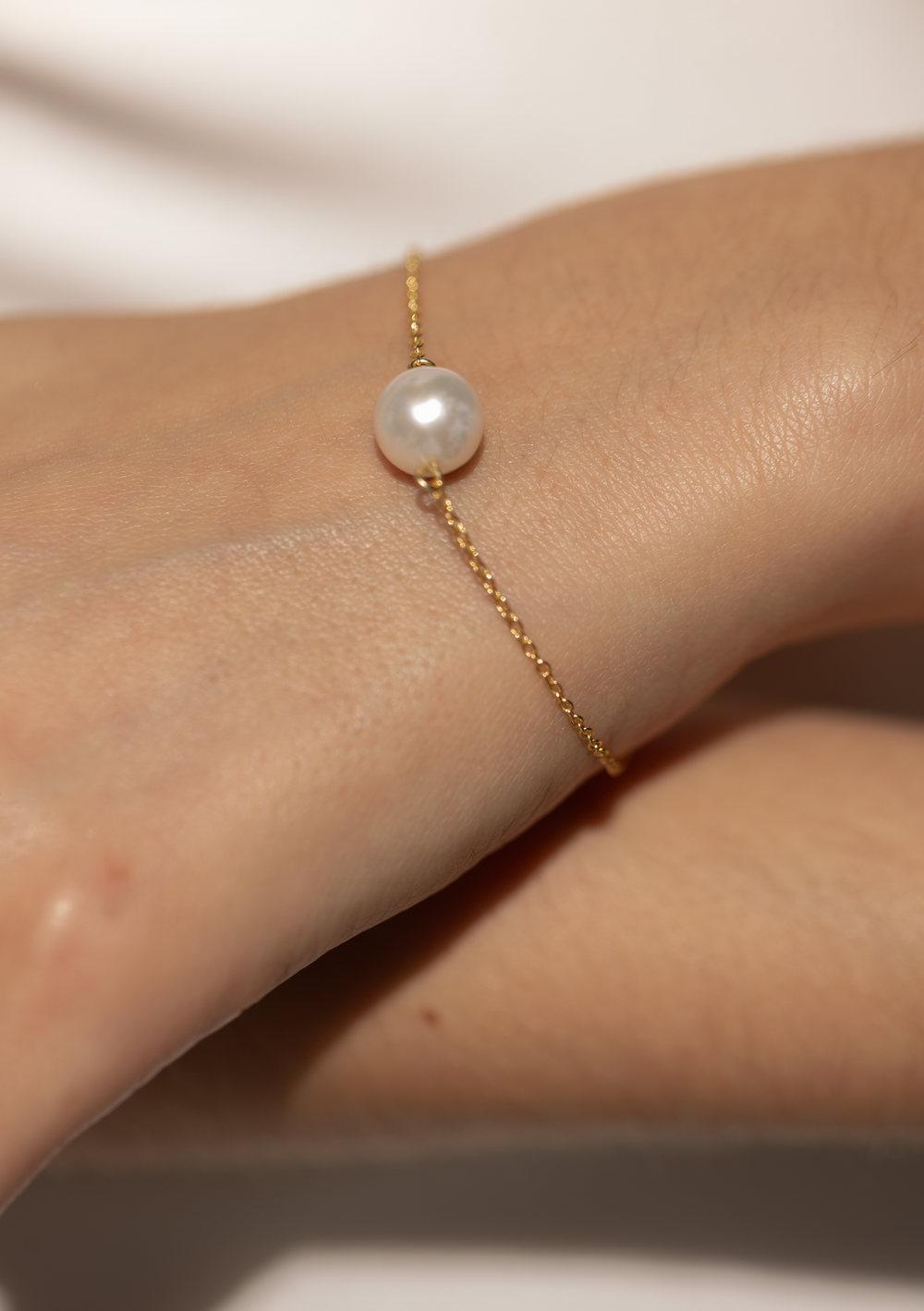 Gold bracelet with a pearl on a wrist against a neutral background