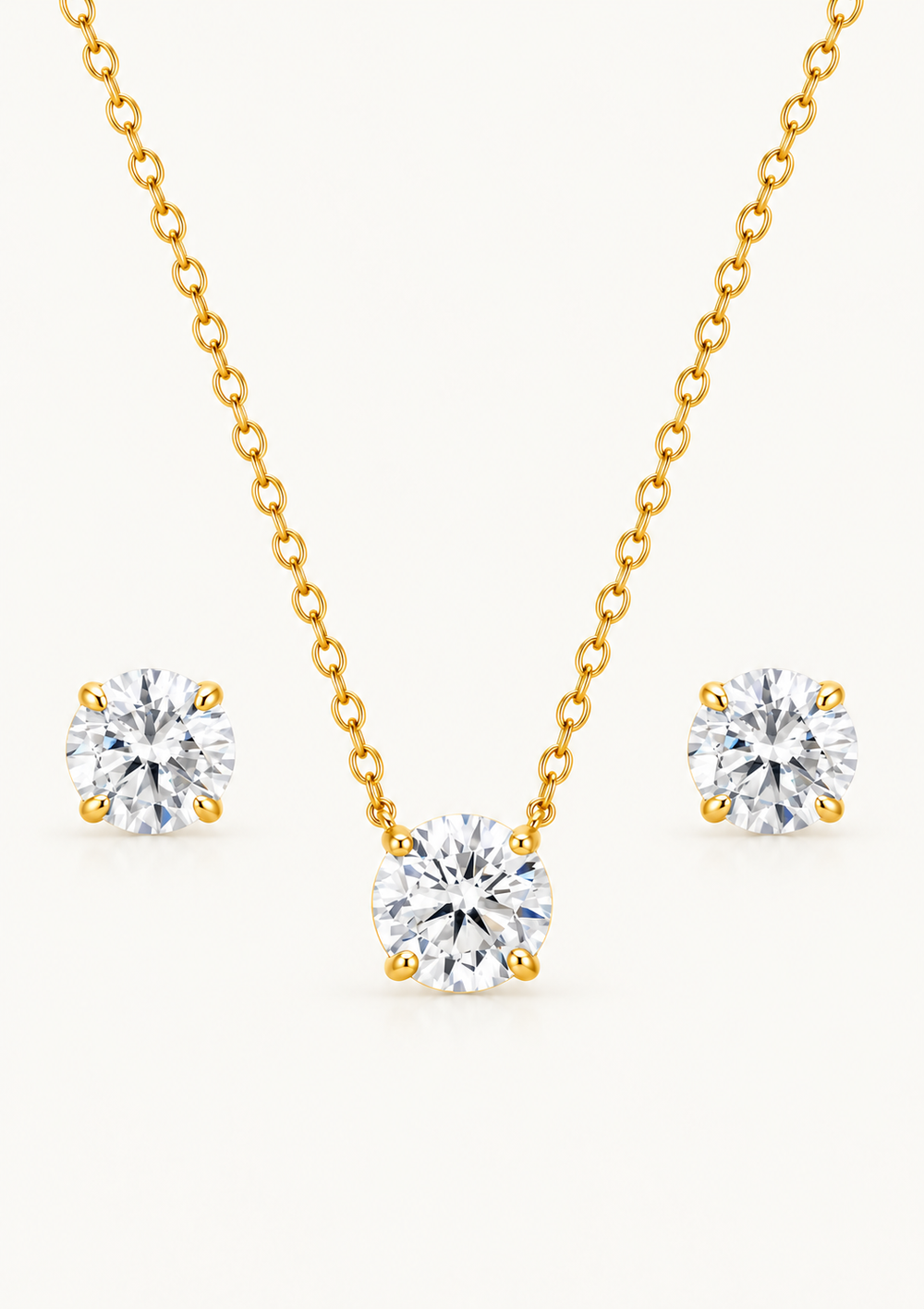 A gold necklace and matching stud earrings set with three round-cut clear gemstones, displayed on a clean off-white background.