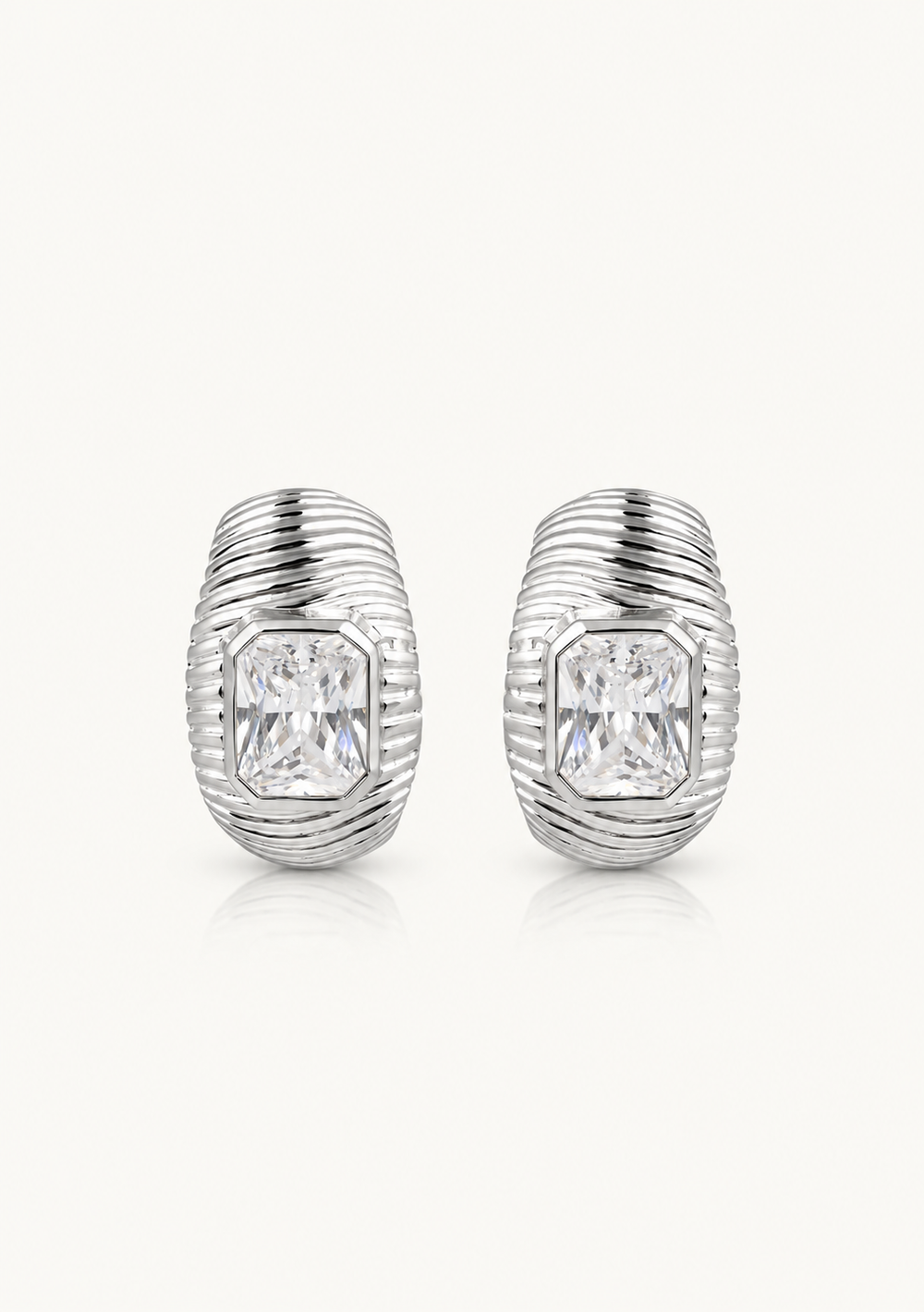 A pair of silver-toned hoop earrings with a textured, ribbed design and a clear rectangular emerald-cut gemstone in the center of each earring, set against a plain off-white background.