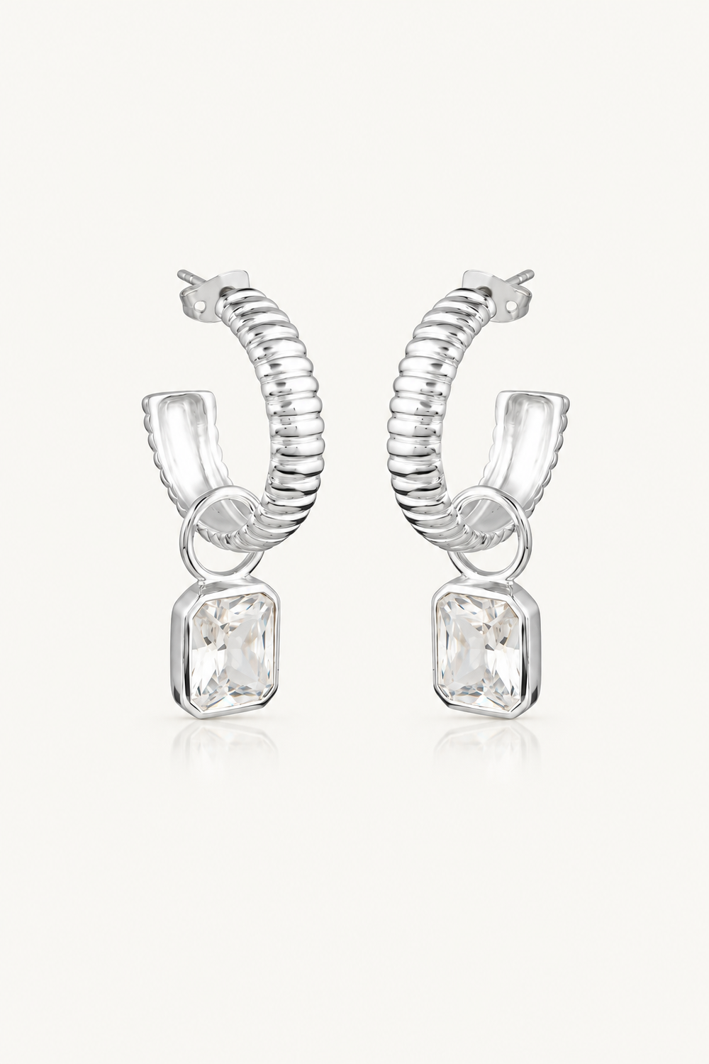 A pair of silver huggie hoop earrings with a textured, snake-like coiled design and a clear rectangular gemstone dangling from each earring, set against a light off-white background.