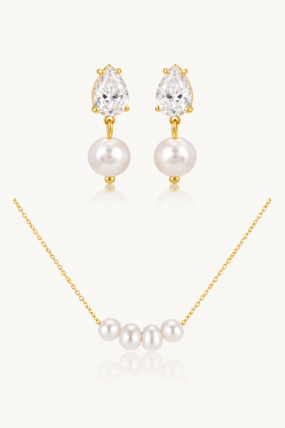 A gold jewelry set featuring a necklace with four white pearls and matching drop earrings with pear-cut clear stones and white pearls, displayed on a light cream background.