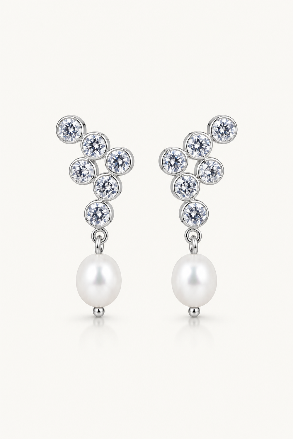 A pair of silver-tone pearl drop wedding earrings featuring a cluster of clear round-cut stones at the top and a single white pearl dangling below, set against a light cream background.