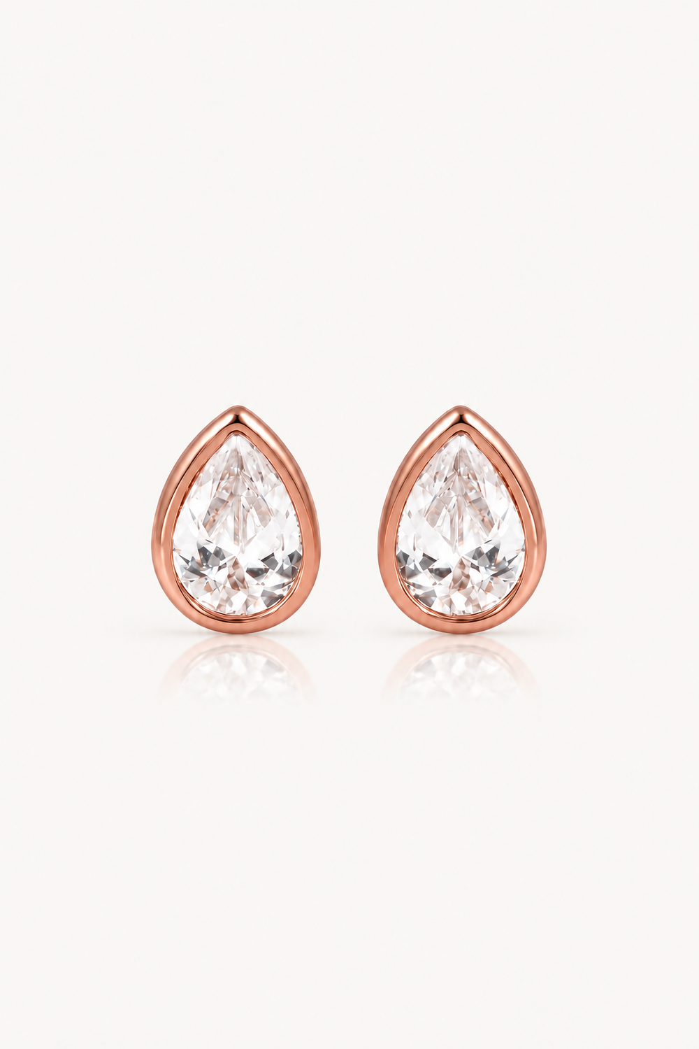 A pair of teardrop-shaped stud earrings with clear faceted gemstones in rose gold settings, displayed on a clean white background with a soft reflection below.
