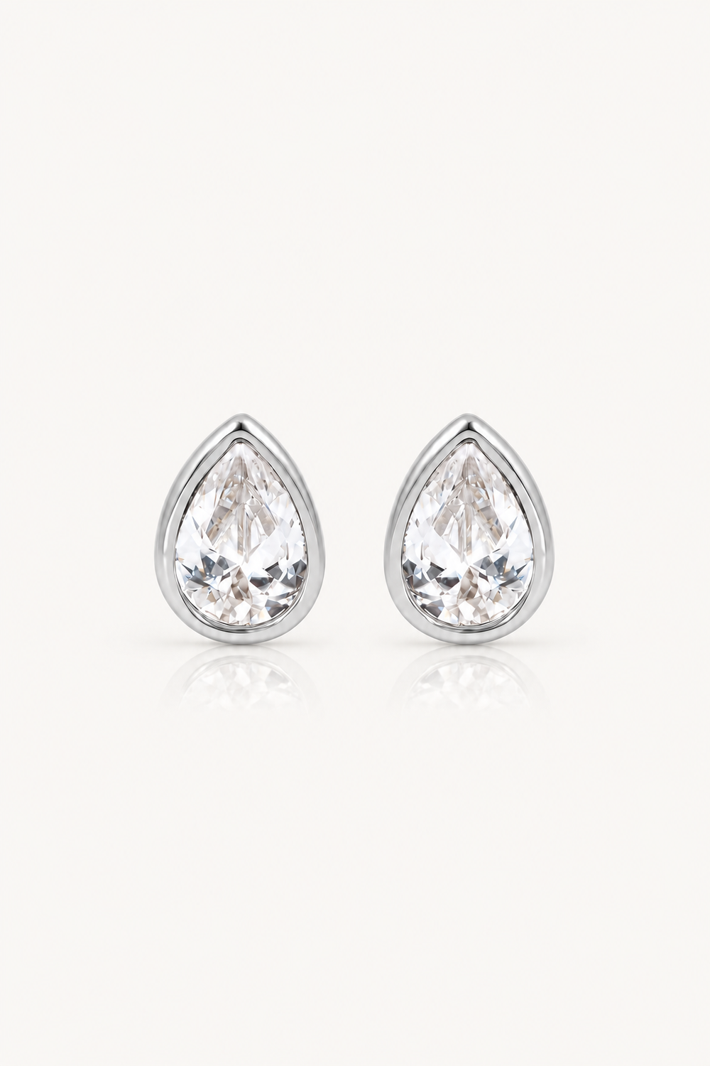 A pair of pear-shaped stud earrings with clear teardrop-cut gemstones in silver-toned settings, shown on a clean off-white background with a soft reflection below.