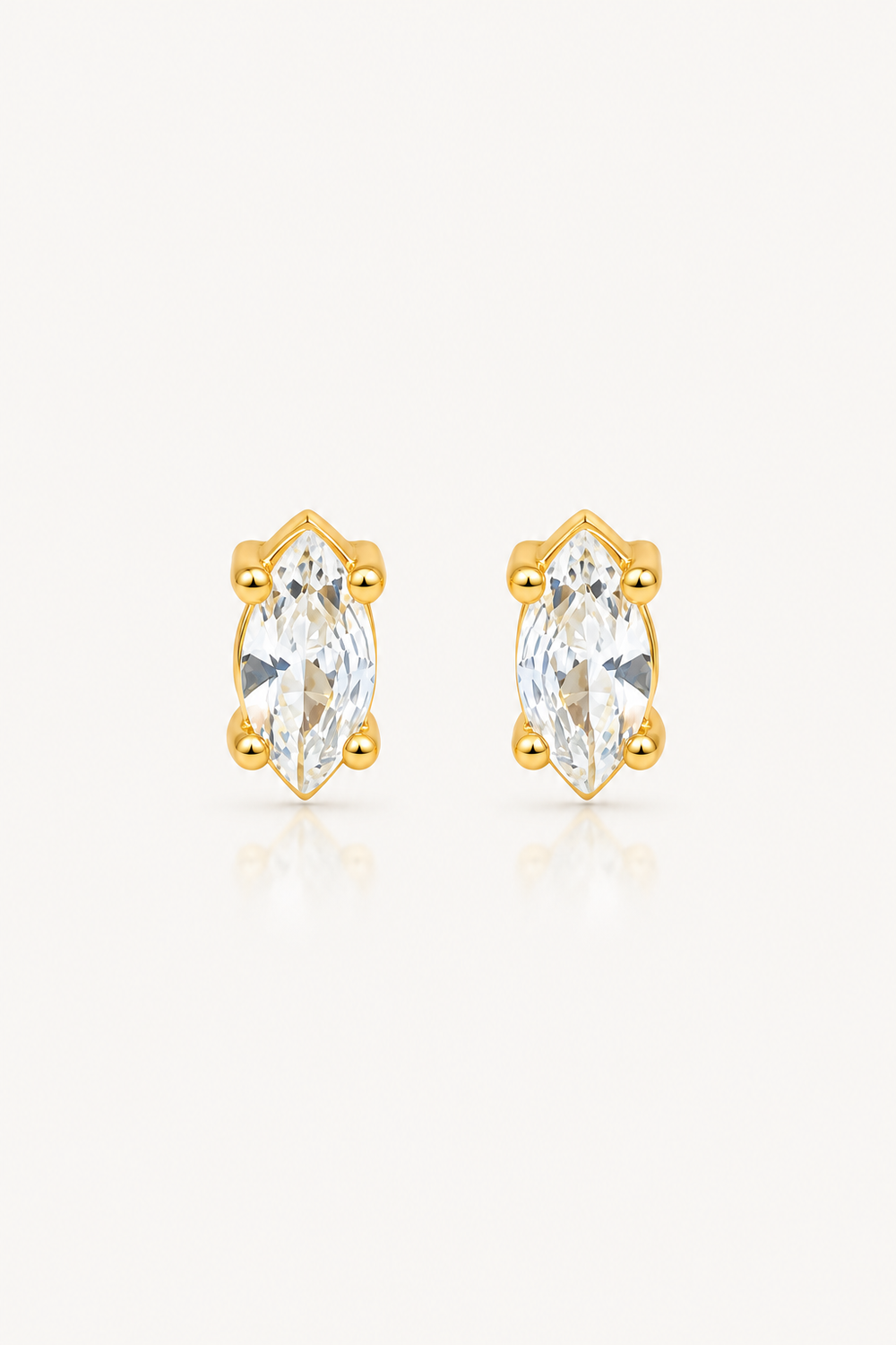 A pair of gold stud earrings with marquise-cut clear gemstones in a prong setting, shown on a clean off-white background.