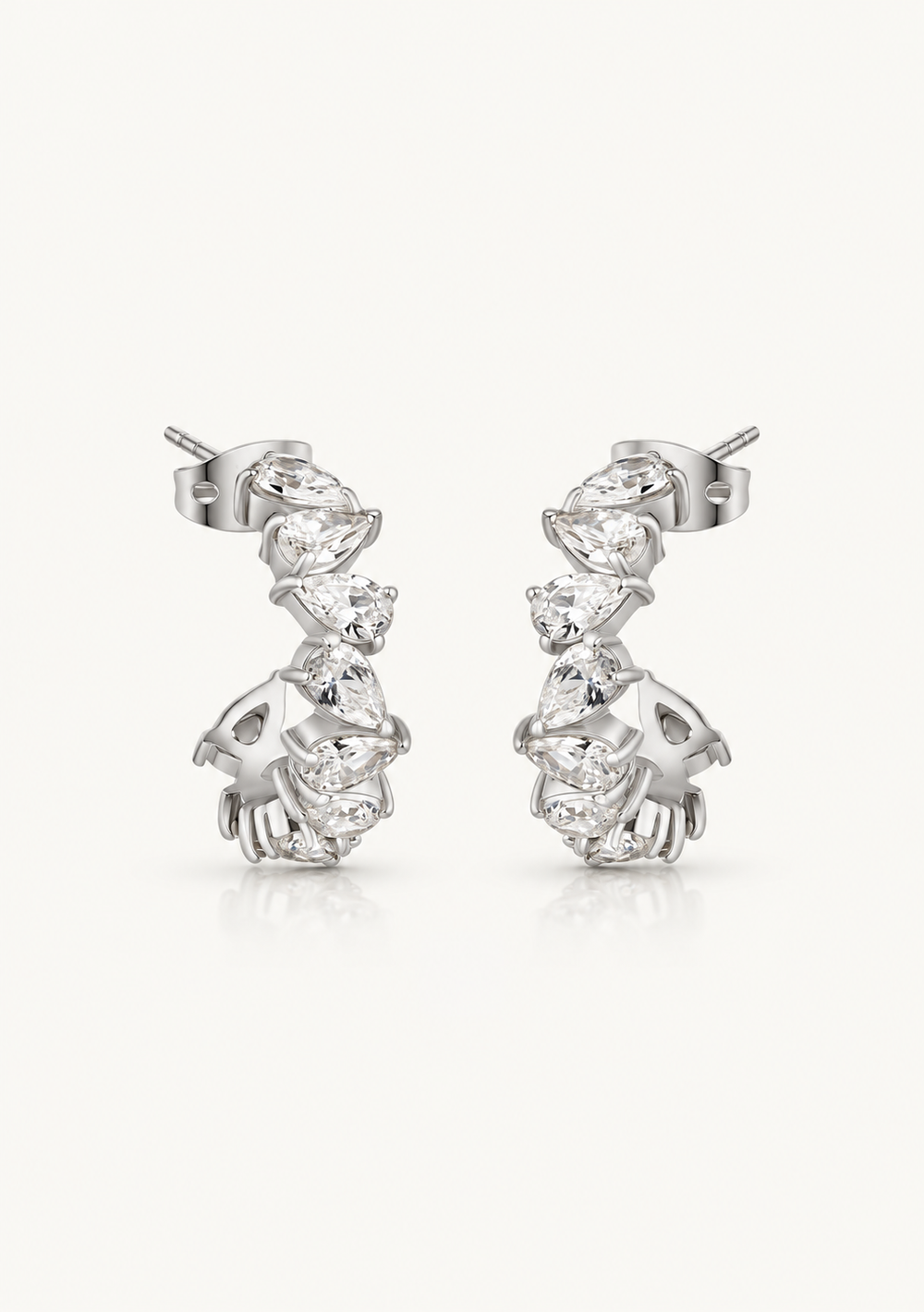 A pair of silver-toned dangle earrings with a series of clear gemstones, photographed on a clean, light off-white background.