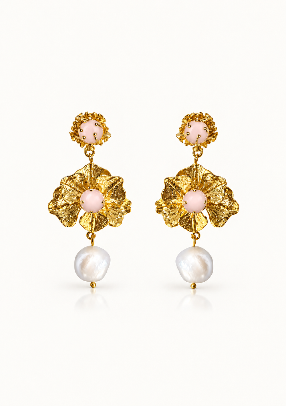 A pair of gold-tone dangle earrings featuring textured flower-shaped metalwork, pale pink oval stones, and dangling baroque-style white pearls, shown on a clean white background.