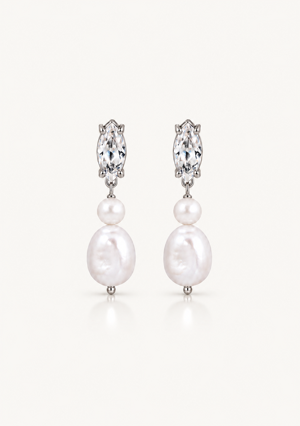 A pair of silver drop earrings featuring a marquise-cut clear crystal and two white freshwater pearls of varying sizes, set against a clean off-white background.