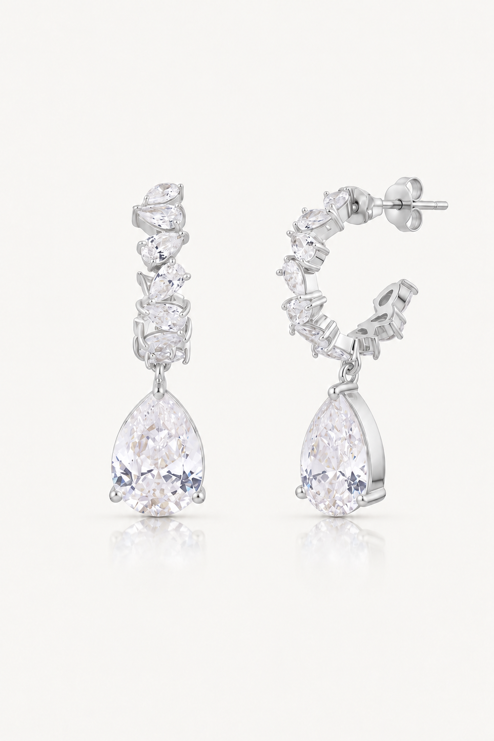 A pair of silver-toned drop earrings featuring a cluster of clear marquise-cut stones above a larger pear-cut clear stone, shown on a light gray background.