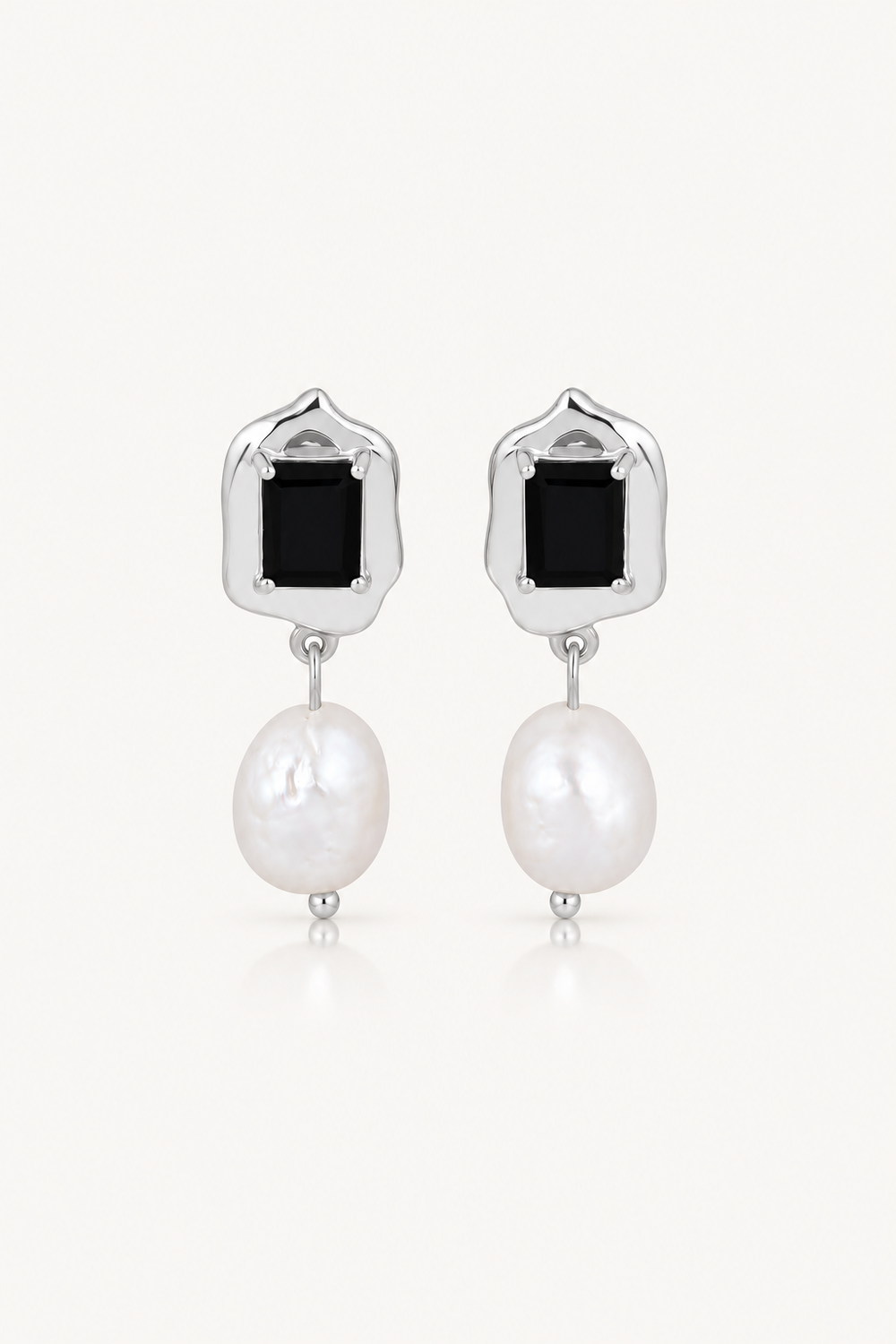 A pair of silver drop earrings featuring a rectangular black onyx stone and a dangling baroque white pearl, set against a clean off-white background.