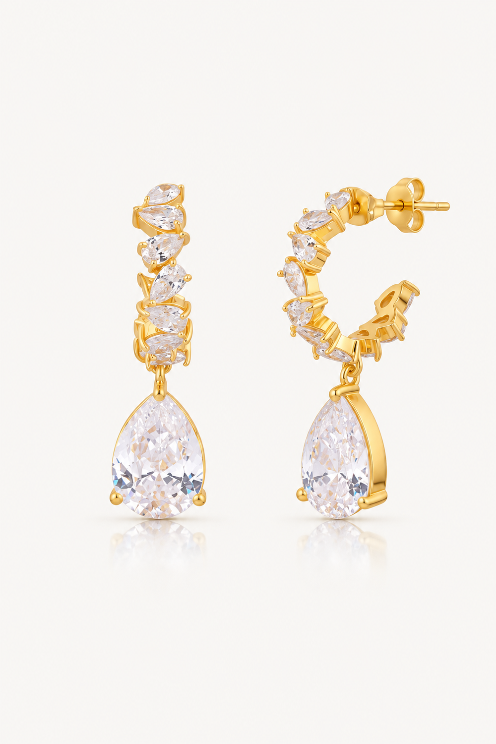 A pair of gold hoop earrings with a dangling teardrop-shaped clear gemstone and smaller clear stones along the hoop, shown on a light gray background.