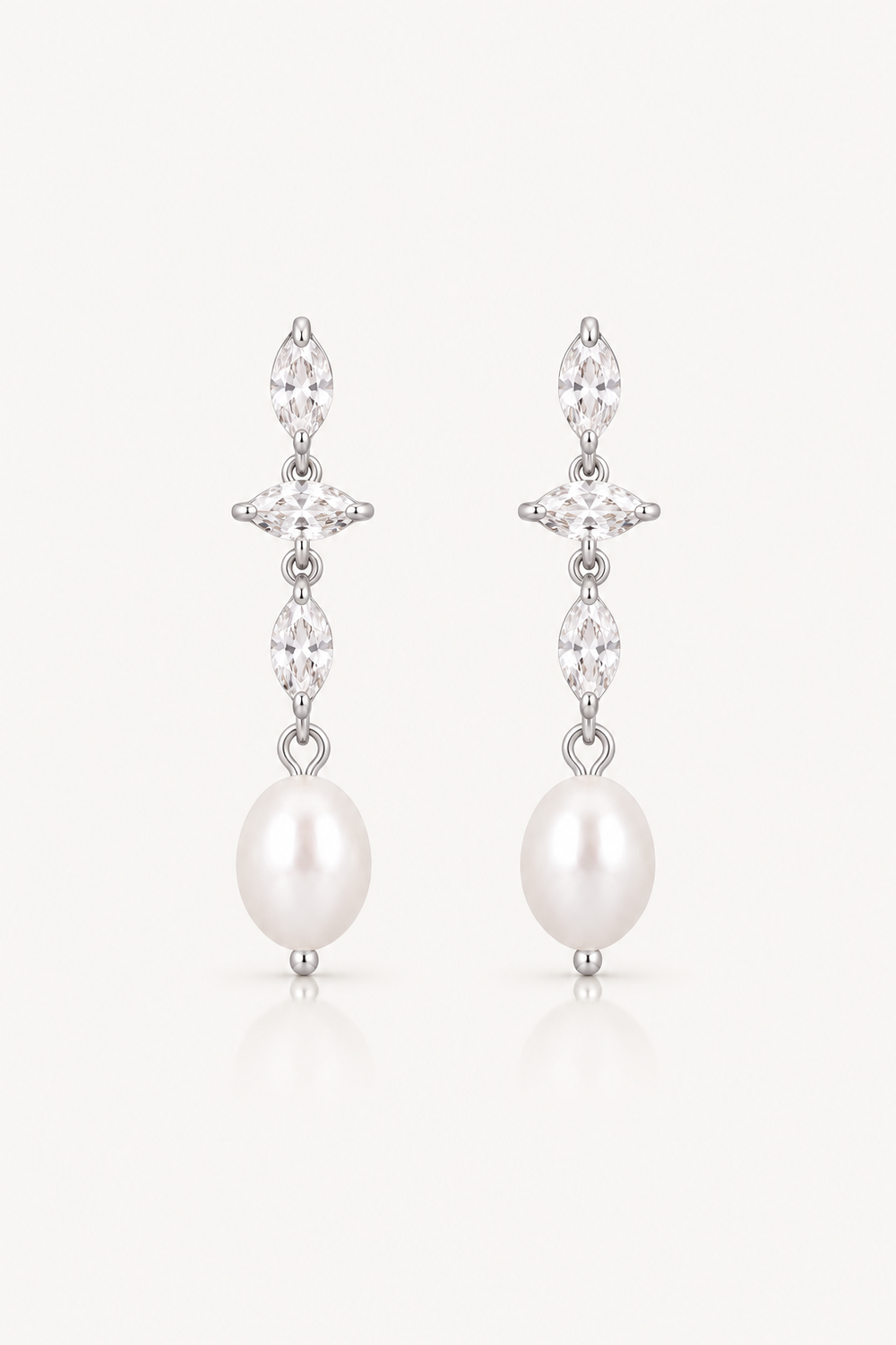 A pair of silver-tone drop earrings featuring marquise-cut clear stones and a large white pearl at the bottom, set against a clean off-white background.