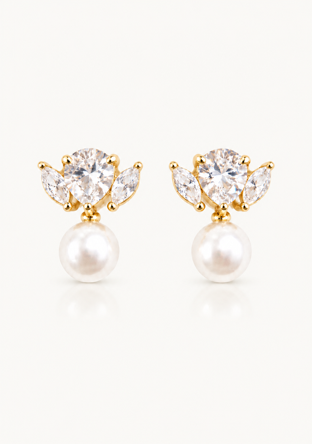 A pair of gold stud earrings featuring a cluster of clear gemstones in a floral-like arrangement above a round white pearl, shown on a clean off-white background.
Crystal pearl bridal earrings.